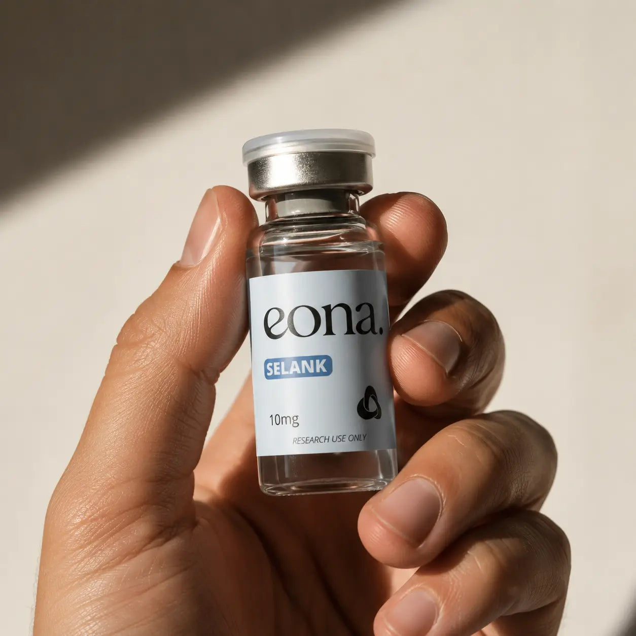 Nahaufnahme einer männlichen Hand, die ein transparentes EONA-Fläschchen mit der Aufschrift „Selank 10 mg“ hält. Warmes, direktes Sonnenlicht erzeugt klare Schatten auf dem hellen, neutralen Hintergrund.